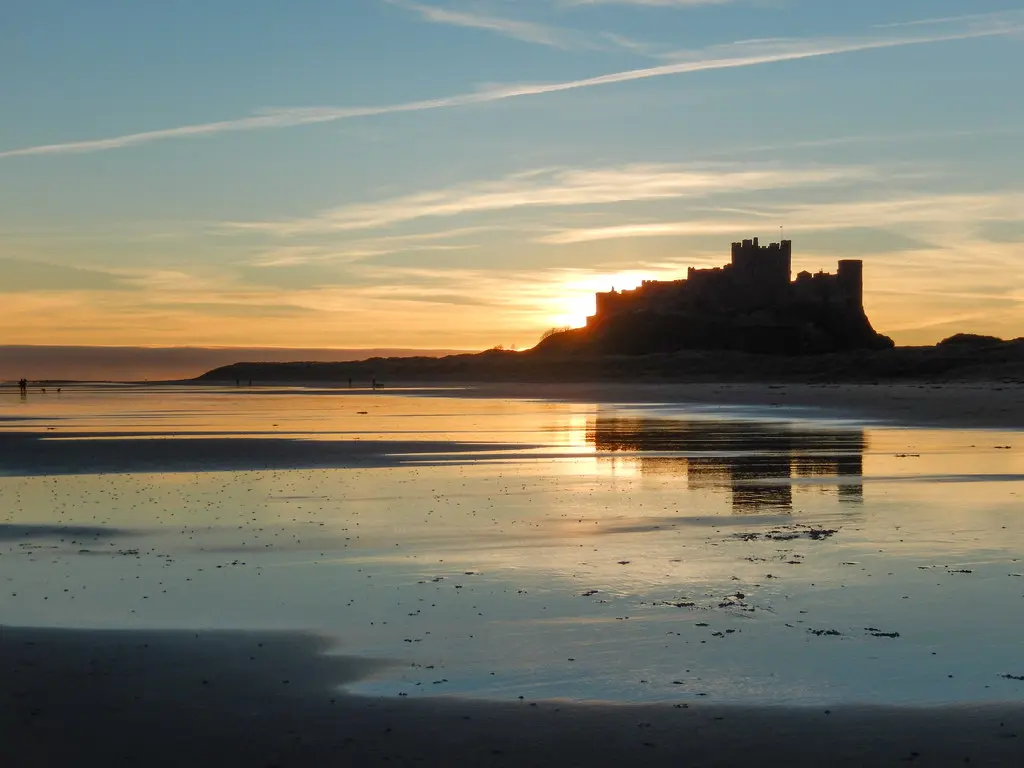 Sunrise behind a silhouetted castle and reflected in water on a sandy beach