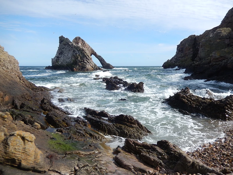 A rocky cove containing a rock arch that is curved like a fiddle’s bow