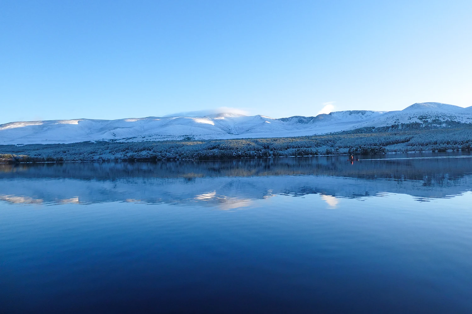 Blue sky and snowy mountains reflected in a loch