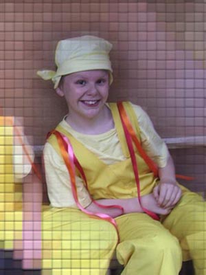 Boy smiling in a yellow costume; the background is pixellated