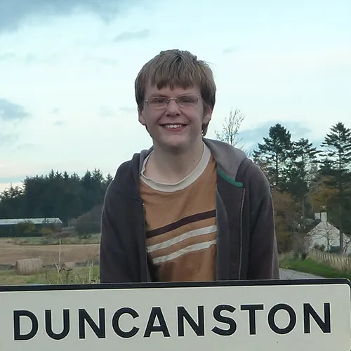 Me aged fourteen behind a sign for Duncanston village